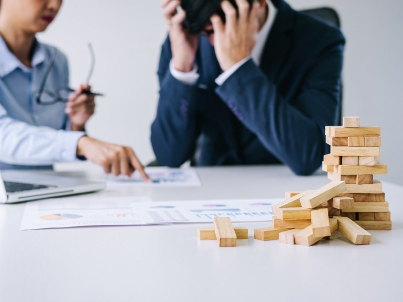 Dois profissionais analisando relatórios com pilha de peças de madeira caídas sobre a mesa, representando erros e falhas em vendas B2B.