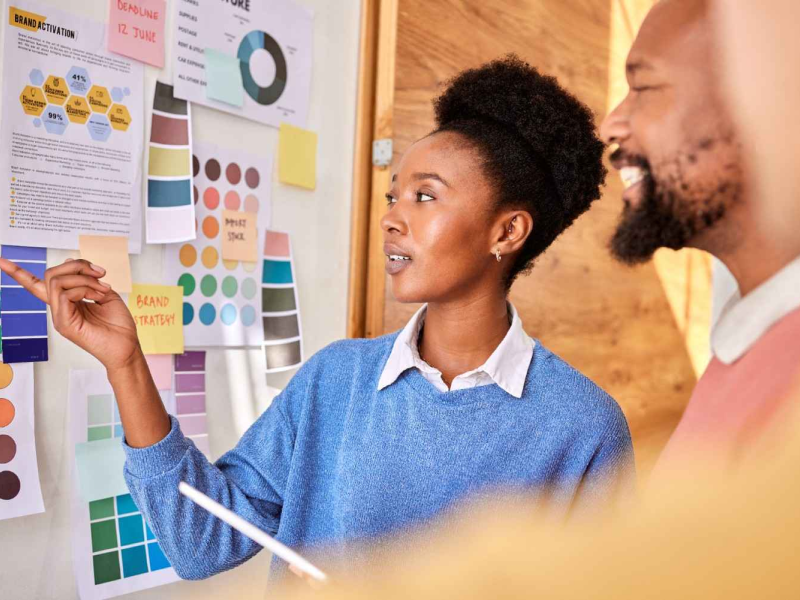 Profissionais analisando um painel de planejamento com gráficos e post-its coloridos, em uma reunião de produto.